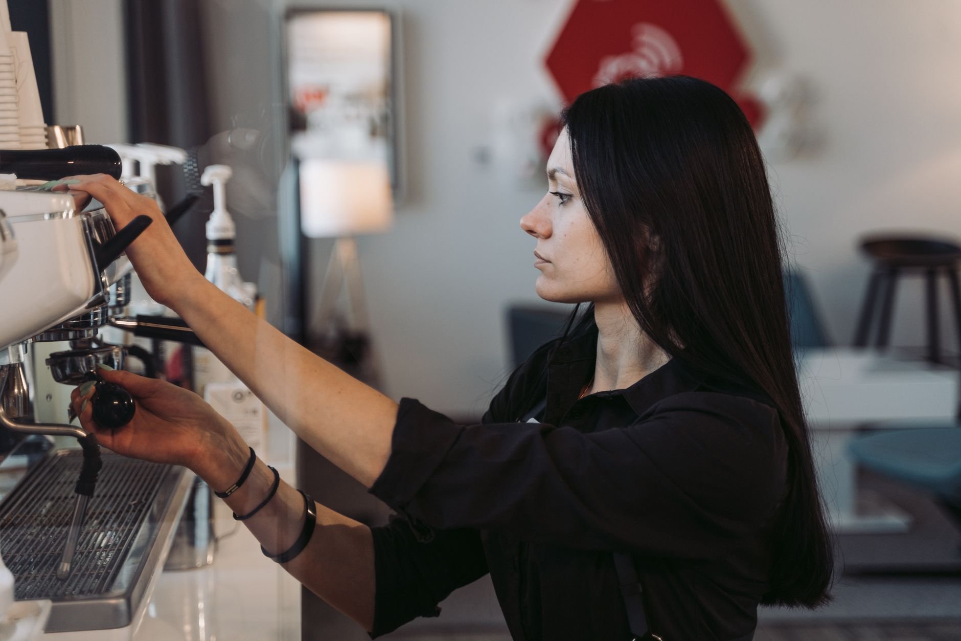 A female barista prepares coffee using an espresso machine in a cozy cafe.